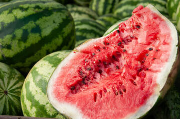 Close-up of a ripe watermelon cut in half, revealing juicy red flesh and black seeds, surrounded by whole green-striped watermelons. Fresh and vibrant image good for food advertising, summer concept