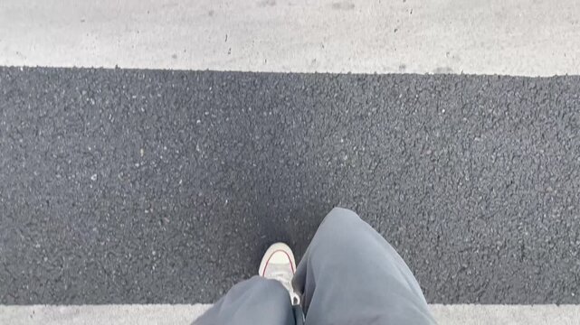 POV. First - person view of walking on a zebra crossing, wearing light - colored wide - leg pants and classic white sneakers.
