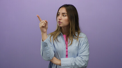 Young blonde woman points assertively against an isolated purple wall in a confident expression.