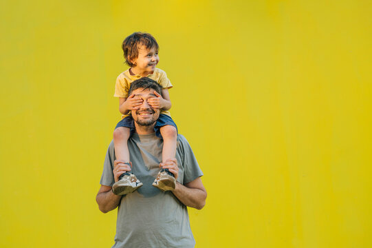 Father carrying son on shoulders against yellow background outdoors