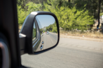 Reflective View of a Road and Surrounding Greenery From a Car Side Mirror on a Sunny Day