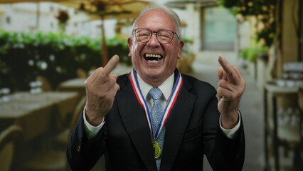 Senior man in suit makes rude gesture while laughing on restaurant terrace, showcasing defiant...