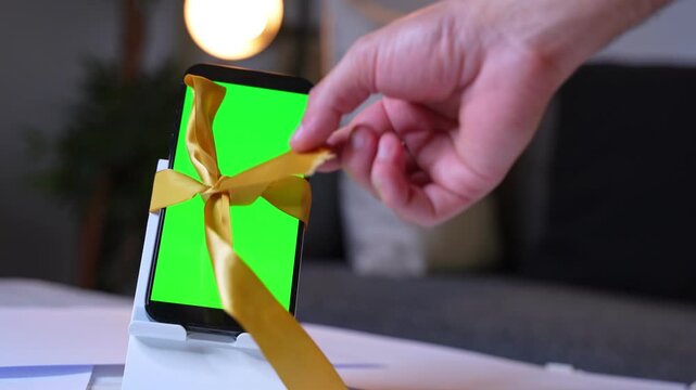 Phone wrapped with golden ribbon on stand featuring green screen. Ideal for unboxing promos, tech gifts, product ads, and celebration content.