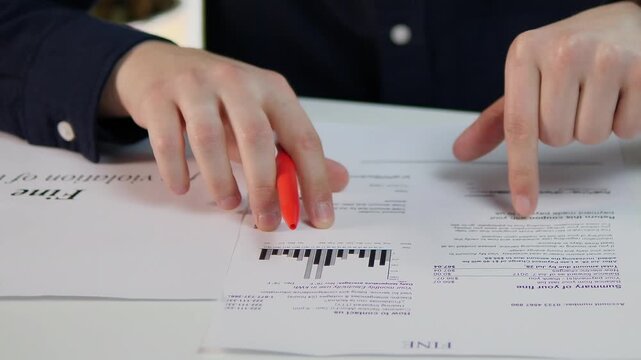 Close-up of a man's hands running his finger over the text of a fine notice, studying it and the reasons for the fine. Fine notice, searching for reasons.