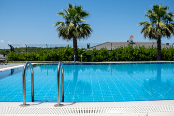 Clear Blue Swimming Pool Surrounded by Palm Trees in a Sunny Outdoor Setting During the Daytime