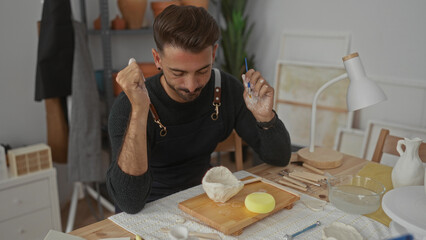 Man shaping raw clay bowl with brush and hand at wooden table in artisan studio; mindful...