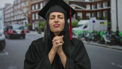 Young hispanic woman in graduation gown looking frustrated on a city street, expressing emotion...