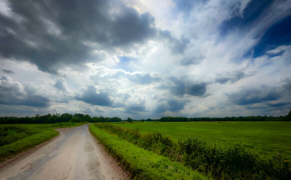 A breathtaking and picturesque view of a winding country road that runs through vibrant green fields under a moody sky