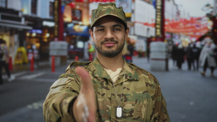Fototapeta premium Man in camouflage uniform extending his right hand forward for a friendly handshake on a bustling street; trust.