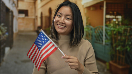 Woman with asian descent holding american flag on city street smiling outdoors in usa, representing cultural diversity and patriotism in urban setting.