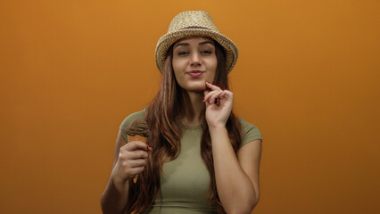 Young woman wearing a hat holds ice cream against orange background, suggesting summer and leisure...