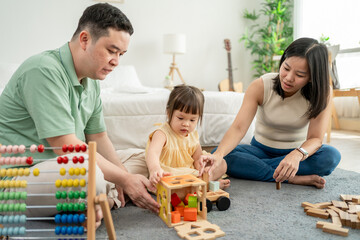 Cheerful kid girl playing with colorful toys with loving parents in house. 