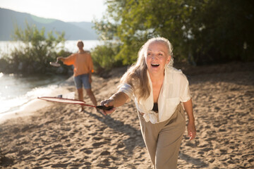 Summer lifestyle portrait senior woman with gray hair playing badminton, having fun in the seashore on sunny summer day.  Enjoying the little things. spends time in nature in summer.  women's friends
