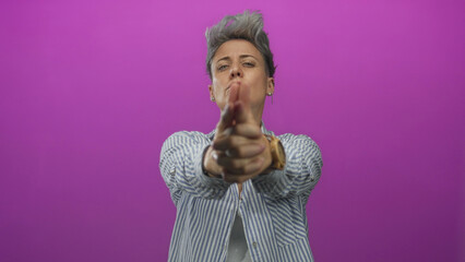 Woman with short gray hair wearing striped shirt makes a finger gun gesture with both hands in a...