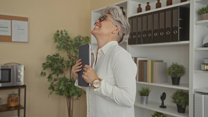 Short haired woman holds tablet and pumps fist in office building; achievement motivation confidence joy.
