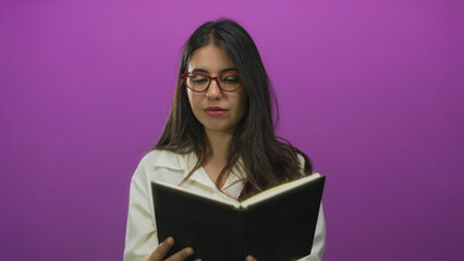 Young woman beckons with finger while holding open book in studio setting with pink walls;...