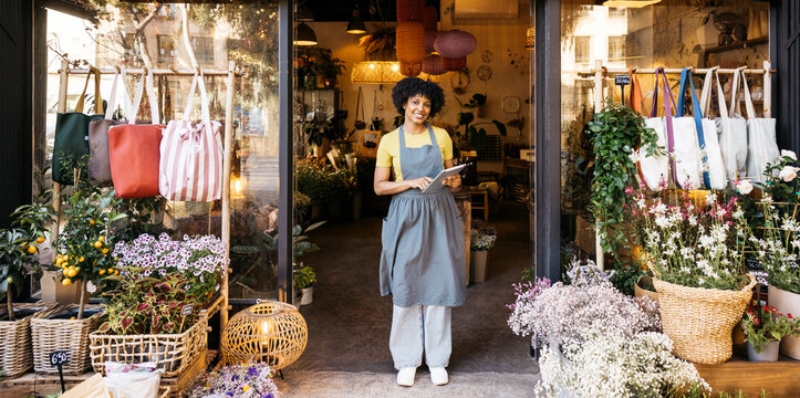 Florist owner holding digital tablet and smiling in front of her flower shop, small business and entrepreneurship concept