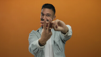 Obraz premium Young man gesturing hashtag symbol against vibrant orange background, showcasing enthusiastic expression and casual style in denim shirt and white t-shirt