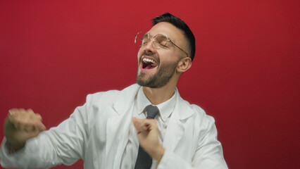 Hispanic man in white coat joyfully dancing against a vibrant red background, exuding happiness and positive energy while showcasing a cheerful moment in life.