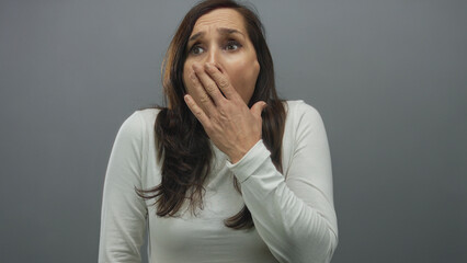 Woman reacting with hand on mouth wearing white shirt in front of grey wall expressing shock or...