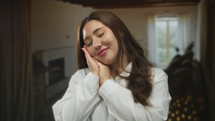 Young hispanic woman with eyes closed and hands pressed to her cheek in a sunlit studio room...