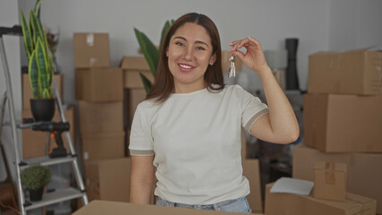 Woman holds keys in building filled with packed moving boxes, a metal ladder and a green houseplant...