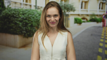 Woman in white dress sticks out tongue on street in front of sunlit building facade; playful attitude.