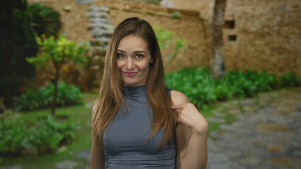 Woman in sleeveless top pointing index finger on cobblestone street of old town with stone wall and...
