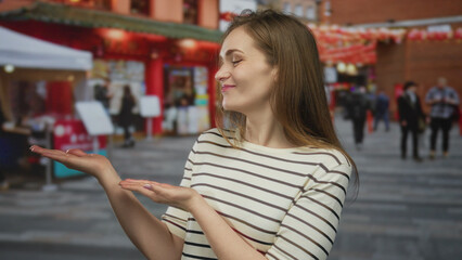 Woman displaying open palms gesture amid passing pedestrians on a crowded urban street outdoors; invitation joy.