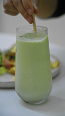 Hand stirring refreshing matcha smoothie with straw in glass on cafe table capturing vibrant creamy texture and inviting ambiance.