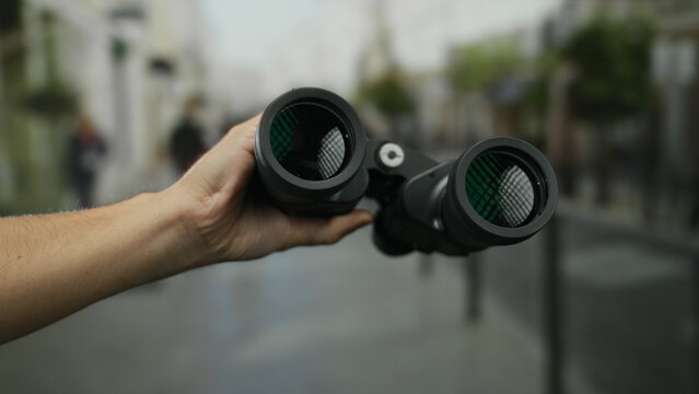 Caucasian man holding binoculars on a street, capturing an outdoor scene in a city setting, highlighting exploration and urban observing dynamics. - Powered by Adobe