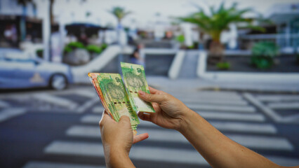 Man holding south african rand on a city street, showcasing currency handling in an urban environment during daytime with visible banknotes and pedestrian crossing.