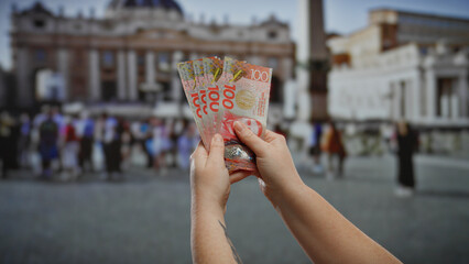 Woman holding new zealand banknotes outdoors with a blurred urban city scene in the background,...
