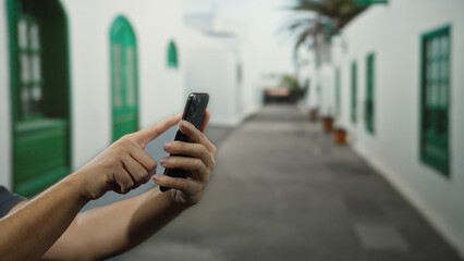 Man using smartphone on city street with green windows, capturing an outdoor urban scene with hands...