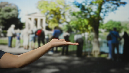 Man's hand extended in outdoor park with blurred crowd and trees in the background showcasing nature and human interaction.