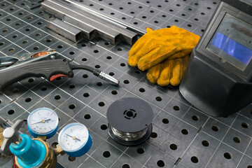 On a metal table there is a set of tools for gas welding, in the middle there is a place for an inscription, gloves and mask