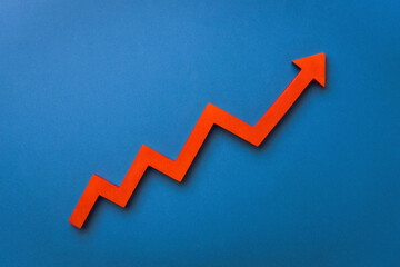 A red upward arrow on a blue background, symbolizing growth or rising trends in finance or economics. Top view, flat lay.