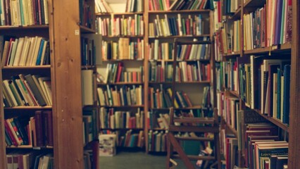 Blurred library interior with defocused bookshelves and numerous text books creating a bokeh effect in an indoor academic setting.