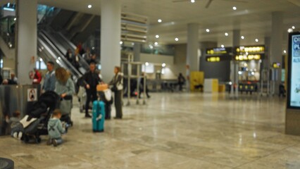 Blurred airport scene with defocused people and luggage in terminal one, featuring busy travelers and family interactions in modern indoor setting.