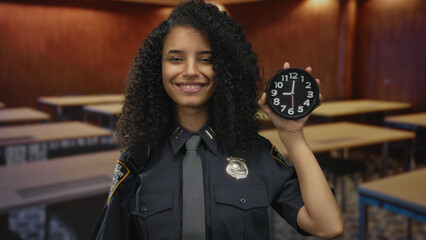 Woman officer in uniform holding clock in classroom demonstrating time management concept indoors.