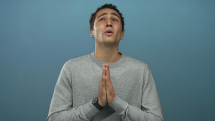 Young hispanic man praying with closed eyes over isolated blue background, expressing hope and...