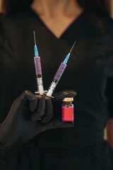  woman hands in gloves wearing black medical suit holding syringes and a nd a small bottle of a cosmetic or medical injectable