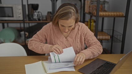 Woman reviewing documents in a cozy office setting with a laptop on the table, creating a focused work environment perfect for productivity and organization.