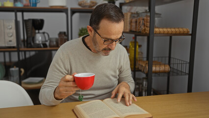 Mature man reading indoors with coffee in hand surrounded by shelves in office setting showing focus and relaxation with warm atmosphere and thoughtful expression.