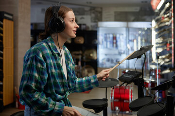 A woman is wearing headphones while playing a drum set in a music store