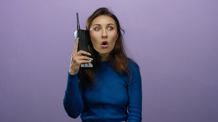 Woman expressing confusion while holding a vintage phone against a purple wall, showcasing emotions...