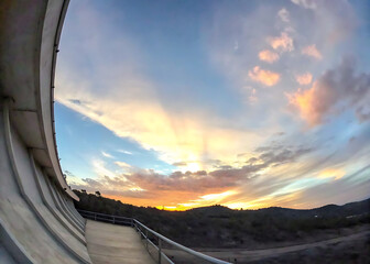 Dramatic sky during sunset with curved clouds, pastel hues, and golden light behind silhouette of hills 