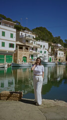 Fototapeta premium Woman standing at cala figuera port, mallorca, surrounded by boats and picturesque mediterranean buildings under a clear blue sky, portraying a tranquil and scenic atmosphere.