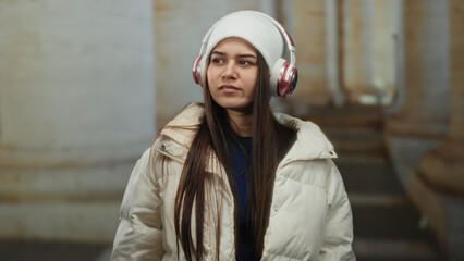 Naklejka premium Woman wearing headphones stands outside an old university immersed in music on a cold day.