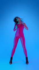 Woman in pink catsuit dancing with high heels against blue background. Concept of music promo,...
